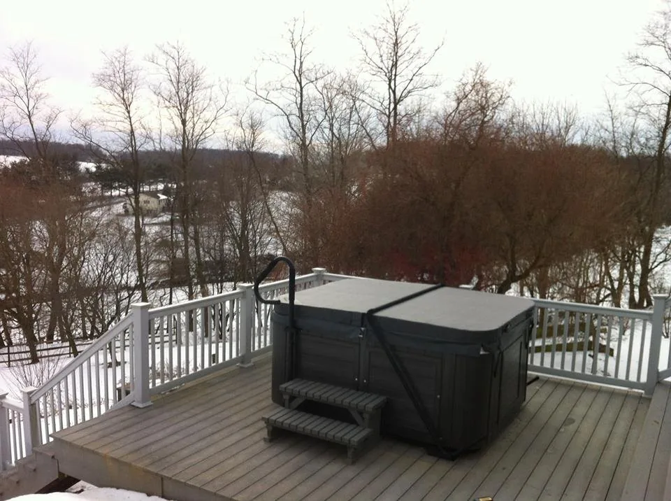 Premium hot tub with dark cabinet beside a pool on a timber deck at golden hour